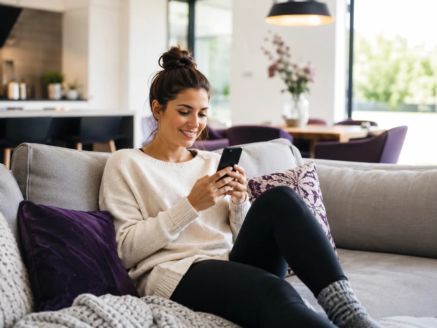 woman sitting on a couch comparing prices on her phone